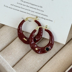 Detail view of burgundy red enamel hoop earrings with gold accents and black gemstone