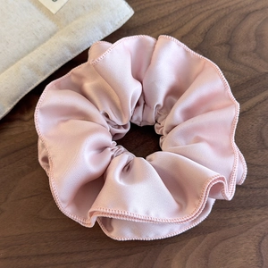 Detail of light pink pleated satin scrunchie showing stitching and soft silk texture