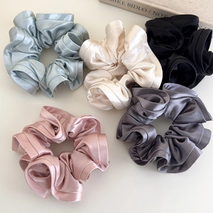 Close-up of five satin silk scrunchies in blue, beige, black, pink, and grey shades