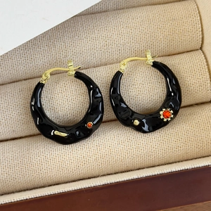 Detail macro view of retro black and gold C-shaped earrings with red gem accents