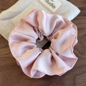 Detail showing the pleated texture and soft luster of a pink satin scrunchie accessory