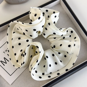 Close-up of cream satin scrunchie with black polka dots and pleated ruffled texture