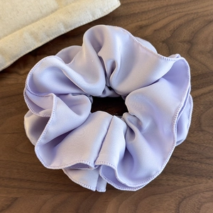 Close-up of lilac ruffled satin hair scrunchie with layered pleats on wood surface
