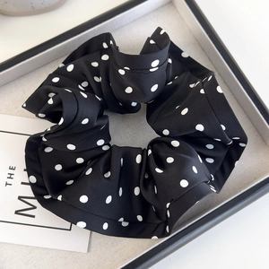 Detailed view of large black satin scrunchie with white polka dots in a premium gift box