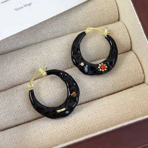 Macro shot of black enamel earrings with orange gemstone and wavy texture in a jewelry box