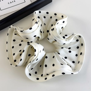 Detailed close-up of white satin polka dot scrunchie with elegant ruffled texture