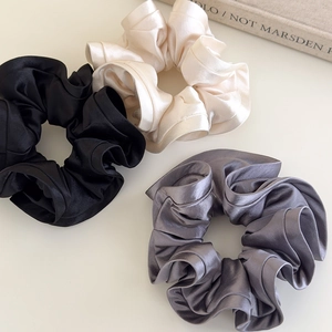 Detailed view of three satin scrunchies in black, cream, and grey with ruffle texture