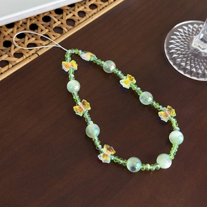 Vue détaillée du bijou de téléphone perlé avec papillon irisé et perles vert clair