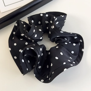 Close-up of French satin black scrunchie with white polka dots and elegant ruffles