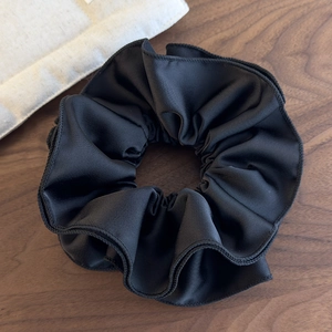 Detail of the glossy black satin fabric and ruched texture on the large scrunchie