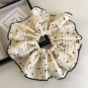 Detailed view of cream satin hair scrunchie with black polka dots and white lace edges
