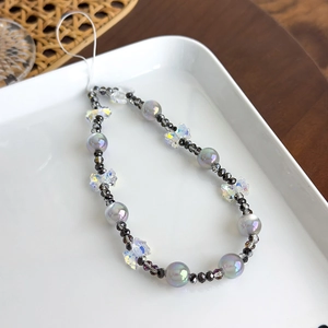 Détail de la dragonne de téléphone en perles irisées avec papillons sur une assiette blanche