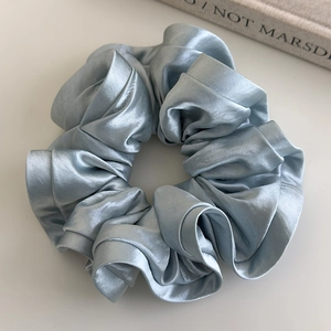 Detail view of ice blue satin scrunchie showing smooth glossy texture and elegant ruffles