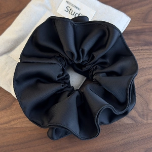 Close-up of large black pleated satin hair scrunchie with layered texture and soft matte finish