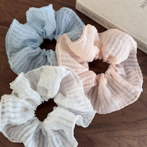 Trois chouchous gaufrés en bleu, rose et blanc disposés sur une surface en bois naturel