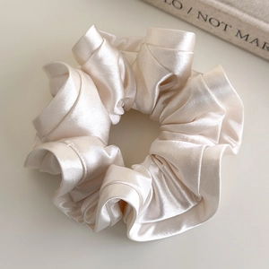 Detail of elegant cream satin scrunchie with smooth pearl finish and soft ruffled fabric