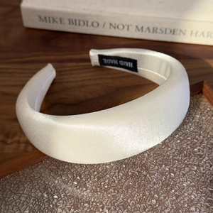 Detailed view of cream satin padded headband with premium silk luster and handmade label