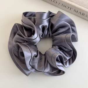 Detail of elegant dark grey satin scrunchie with silky folds and a glossy finish