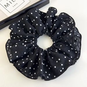 Detail view of oversized black and white polka dot chiffon scrunchie on a white surface