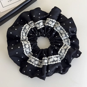 Detail of black satin hair scrunchie with white polka dots and elegant floral lace trim