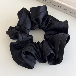 Close-up of a premium black satin scrunchie with elegant ruffled texture on a white surface