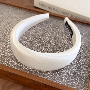 Detail of high-gloss ivory satin headband featuring a black hand made inner label