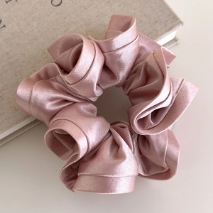 Detailed view of pink satin scrunchie with ruffle edges on a linen book background