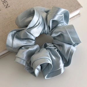 Detailed view of a light blue satin scrunchie with layered ruffles on a book