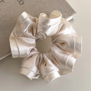 Macro detail of elegant champagne satin silk scrunchie with soft ruffled texture
