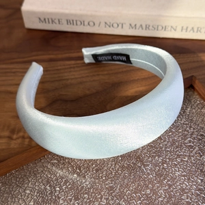 Close-up of light blue padded satin headband with handmade label on wooden background