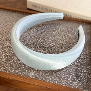 Detail view of wide padded headband in light blue satin finish on glass tray
