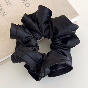 Close-up of black satin scrunchie with elegant ruffled texture and silky shine