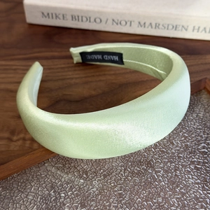 Detail of mint green satin padded headband with handmade label on wooden surface