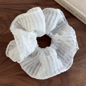 Détail d'un chouchou en organza blanc avec motif quadrillé texturé sur bois