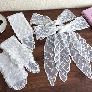 Detail of white lace hair ribbon featuring delicate floral embroidery and scalloped edges