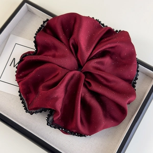 Détail d'un chouchou géant en satin bordeaux avec paillettes et bordure perlée