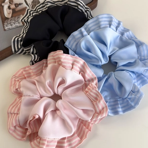 Détail de trois chouchous en satin rose, bleu et noir avec des bords froissés rayés