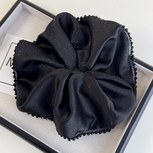 Détail macro d'un chouchou en satin noir avec petites perles et finition scintillante