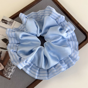 Vue détaillée du chouchou en satin bleu clair avec volants rayés sur un plateau