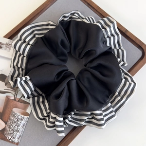 Gros plan d'un chouchou à rayures avec froufrous sur un support gris au style minimaliste