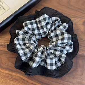 Detail view of black and white checkered scrunchie with pleated mesh edge on wood surface