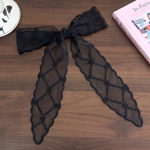 Detail of black lace ribbon with floral embroidery on wooden surface next to a book