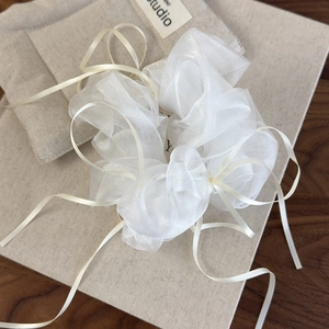 Close-up of white organza scrunchie with cream ribbons on elegant packaging box