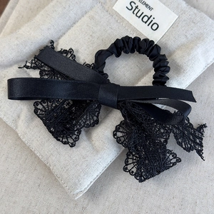 Détail du chouchou nœud en dentelle noire avec texture satinée et bande plissée chic
