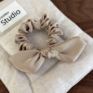 Detailed macro view of champagne satin bow scrunchie with engraved metal charm