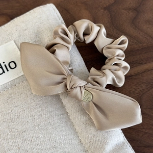 Detailed close-up of champagne satin bow hair scrunchie with a gold engraved metal charm