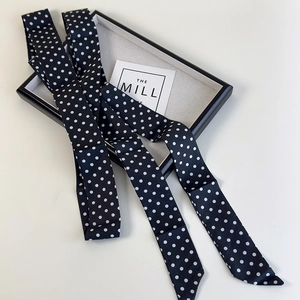 Vue détaillée d'un foulard étroit en satin noir à pois blancs sur un plateau de présentation