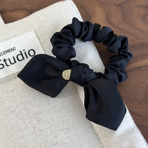 Detail of black satin bow scrunchie with a gold 'MADE WITH LOVE' metal charm decoration
