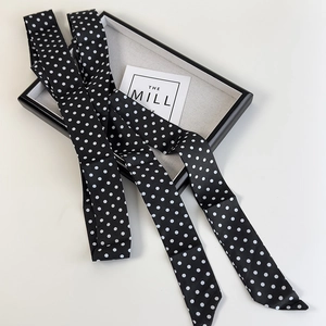 Gros plan sur un foulard en soie à pois noirs et blancs posé sur un plateau blanc