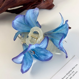 Details einer blauen Lilien-Haarklammer mit Farbverlauf auf dekorativem Holzdekor